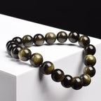 Bracelet obsidienne dorée perles 8 mm posé sur un cube blanc