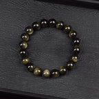 Bracelet obsidienne dorée 8 mm à plat sur ardoise noire