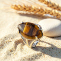 Bague Œil de Tigre réglable en métal argenté, cabochon marquise, posée sur le sable