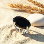 Bague Onyx Noir réglable en métal argenté, cabochon marquise, posée sur le sable