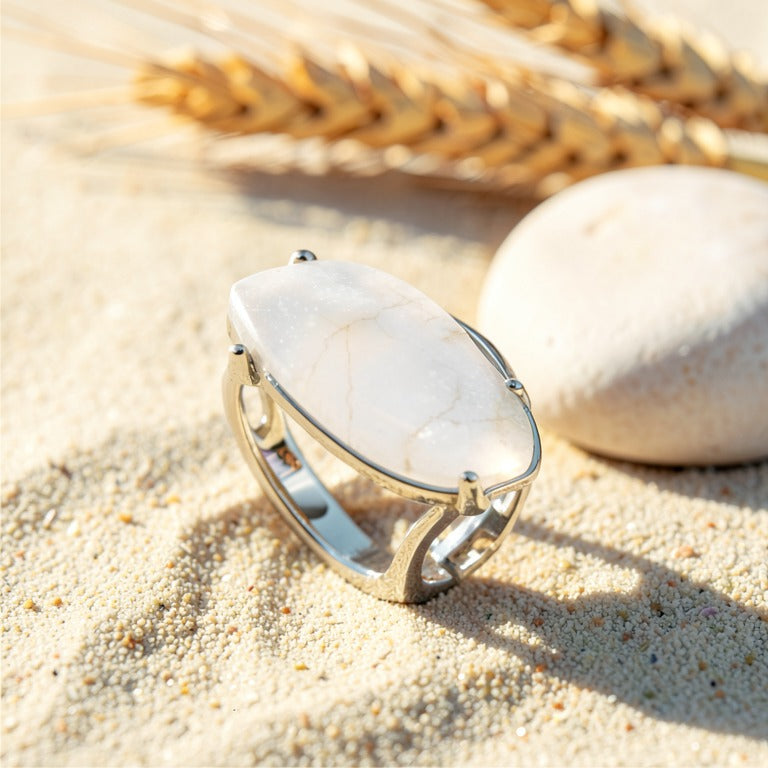 Bague Quartz Blanc réglable en métal argenté, cabochon marquise, posée sur le sable
