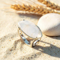 Bague Quartz Blanc réglable en métal argenté, cabochon marquise, posée sur le sable
